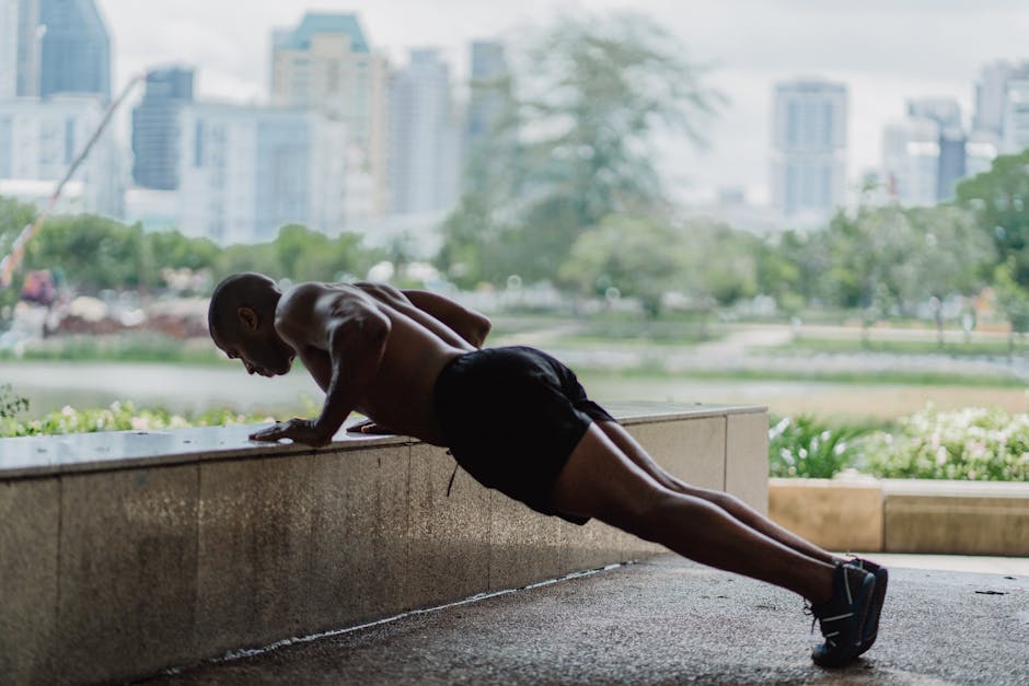 Shirtless man doing push-ups outdoors with city skyline in the background