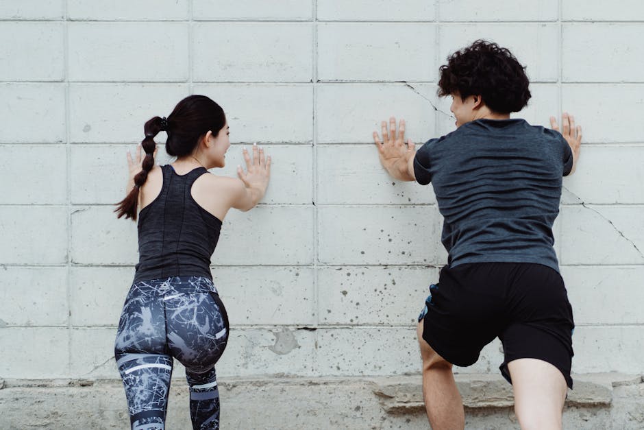 A man and woman push against a wall during an outdoor workout session, focusing on strength and fitness