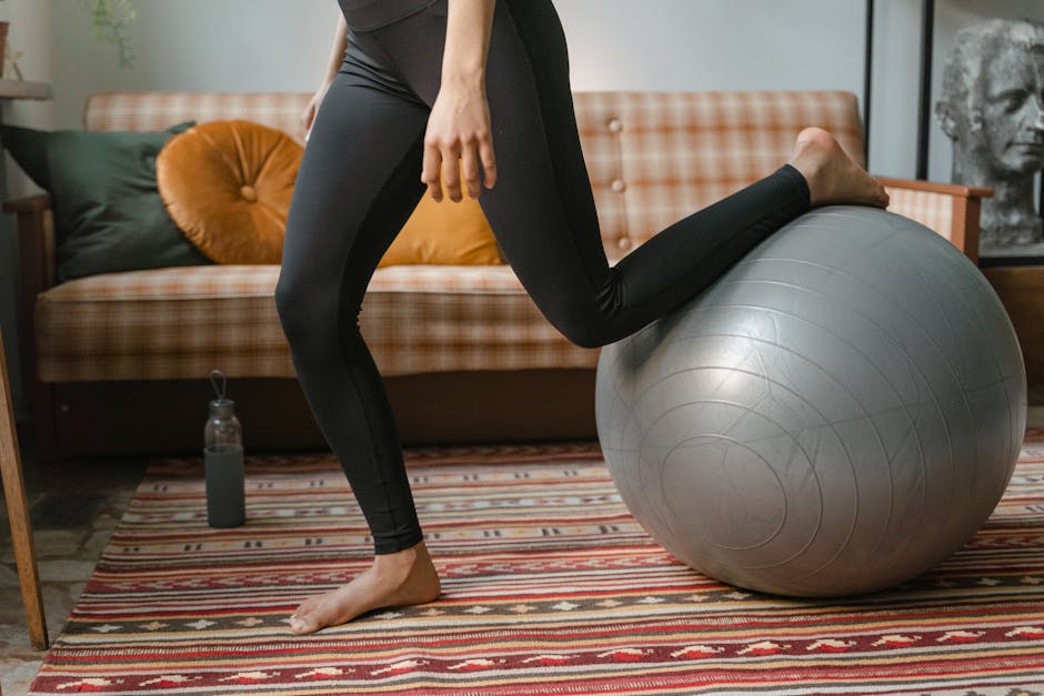 Woman performing home exercise routine using an exercise ball, wearing black leggings